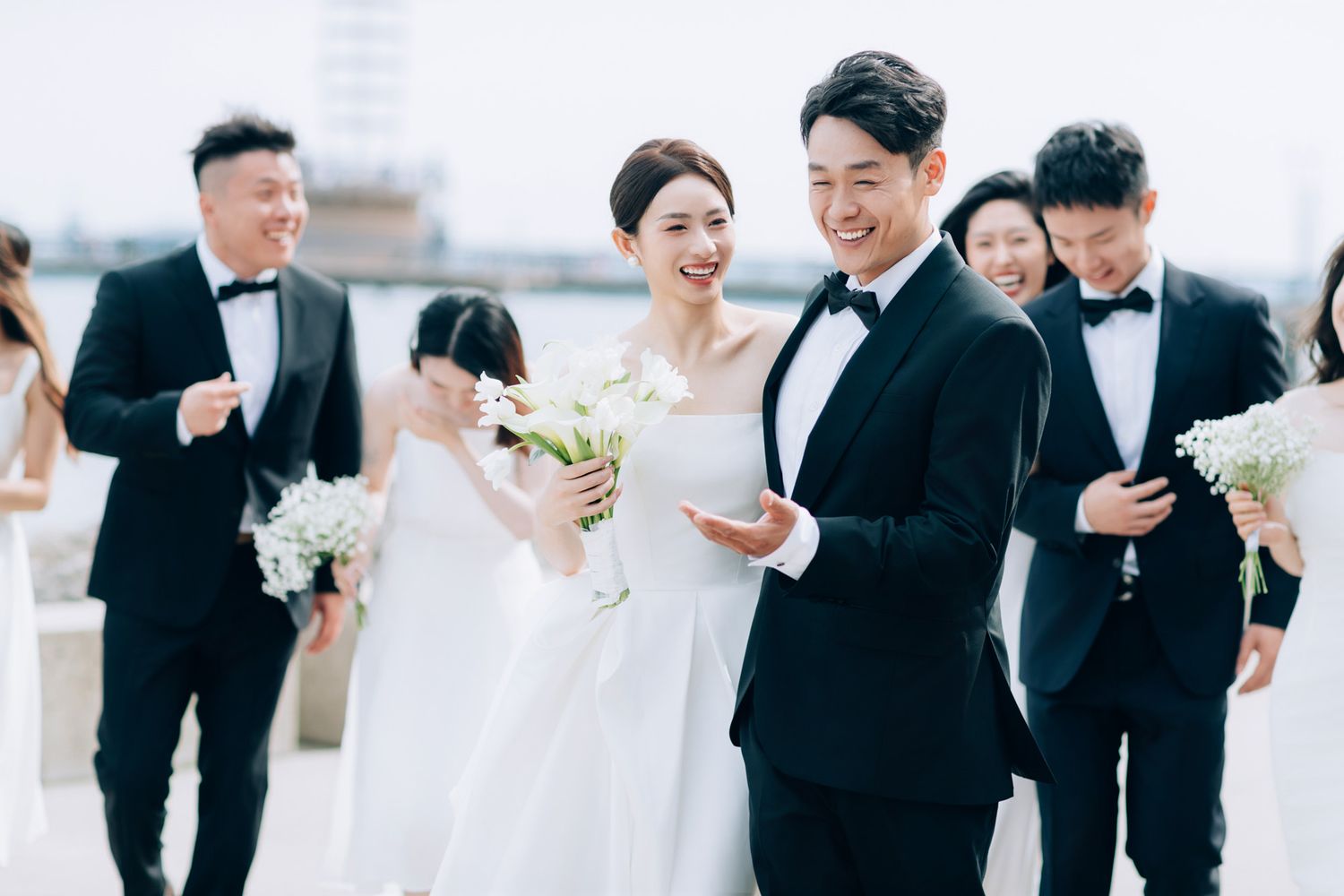 Bride and groom walk with wedding party in black tuxedos and white dresses on rooftop venue.