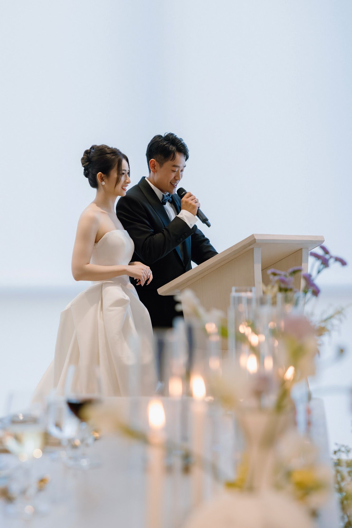 Bride and groom delivering heartfelt speech at podium during elegant candlelit wedding reception.