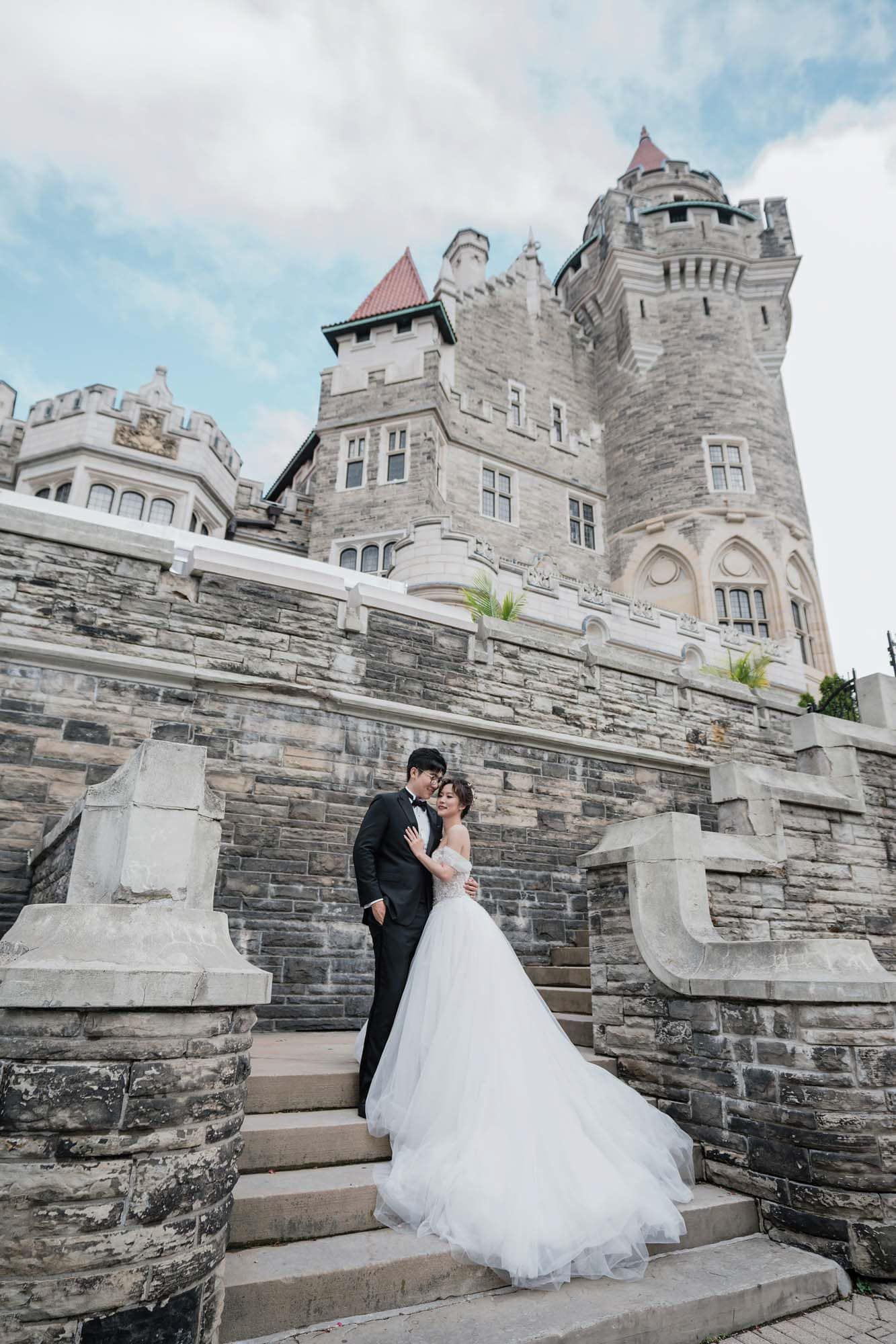 Bride and groom stand on stone steps beneath the towering turrets of Casa Loma.