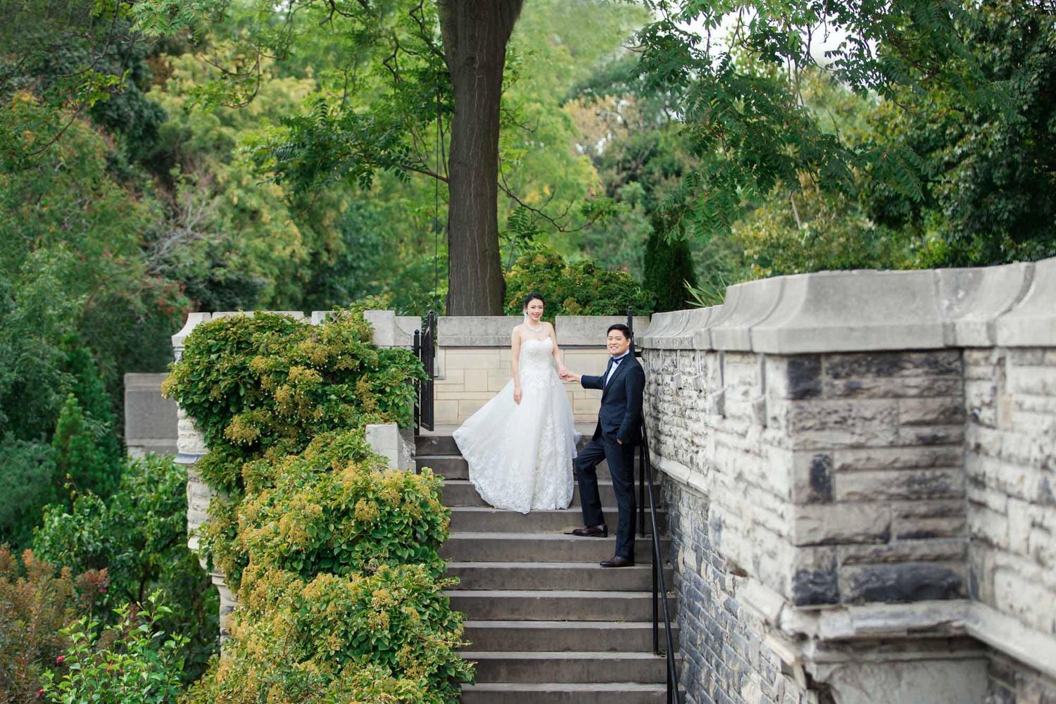 Bride and groom standing on stone staircase surrounded by lush greenery at castle wedding venue.