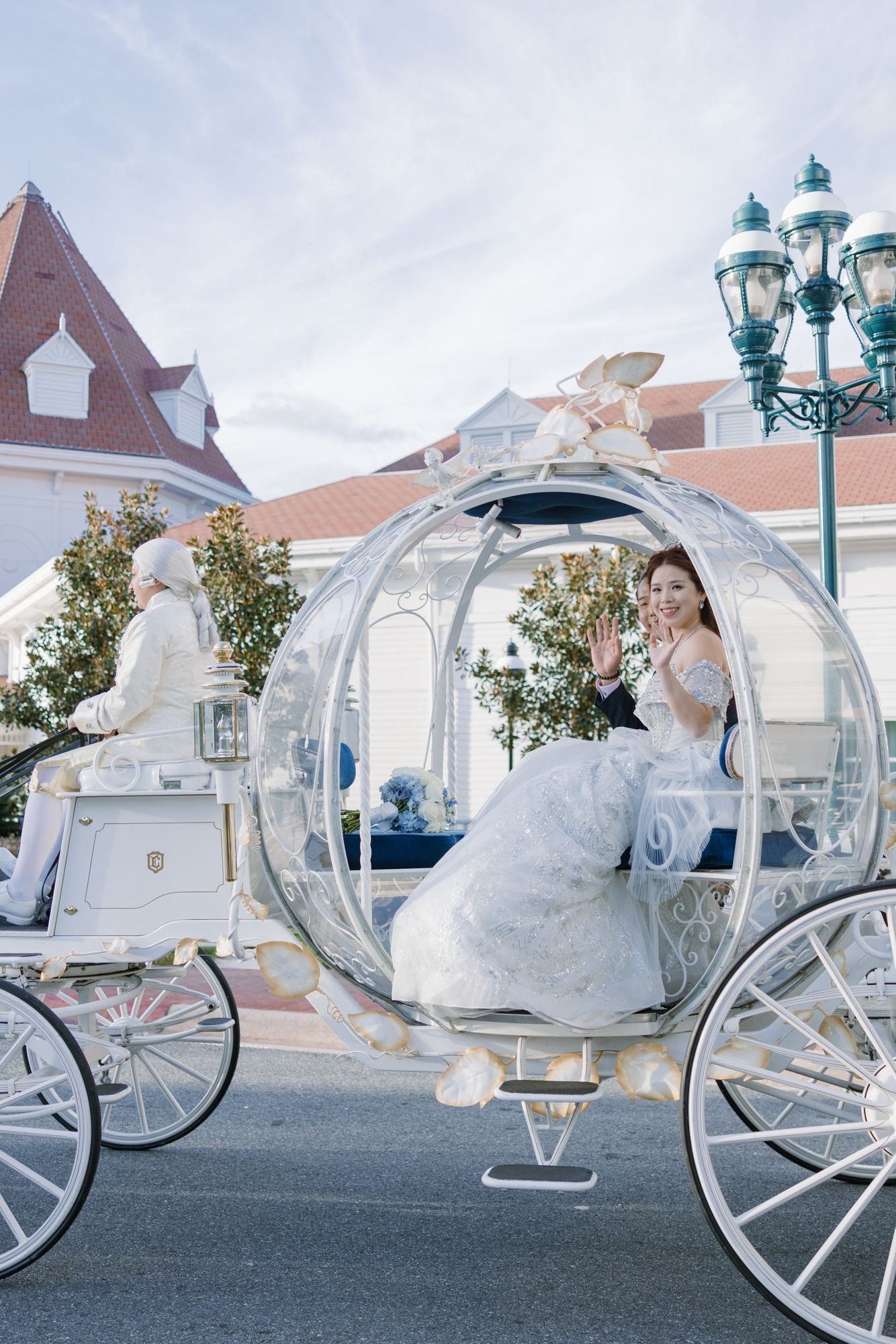 Bride in white gown waves from Cinderella's glass carriage at Disney World wedding.