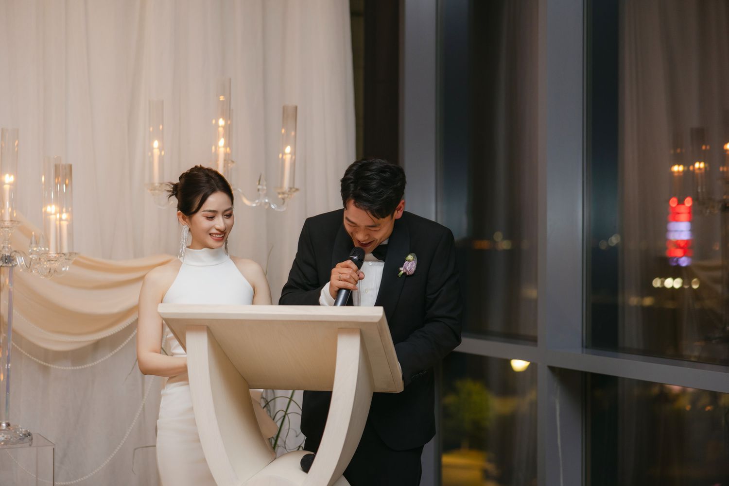 Bride and groom stand together at a white podium giving a speech at their wedding reception.