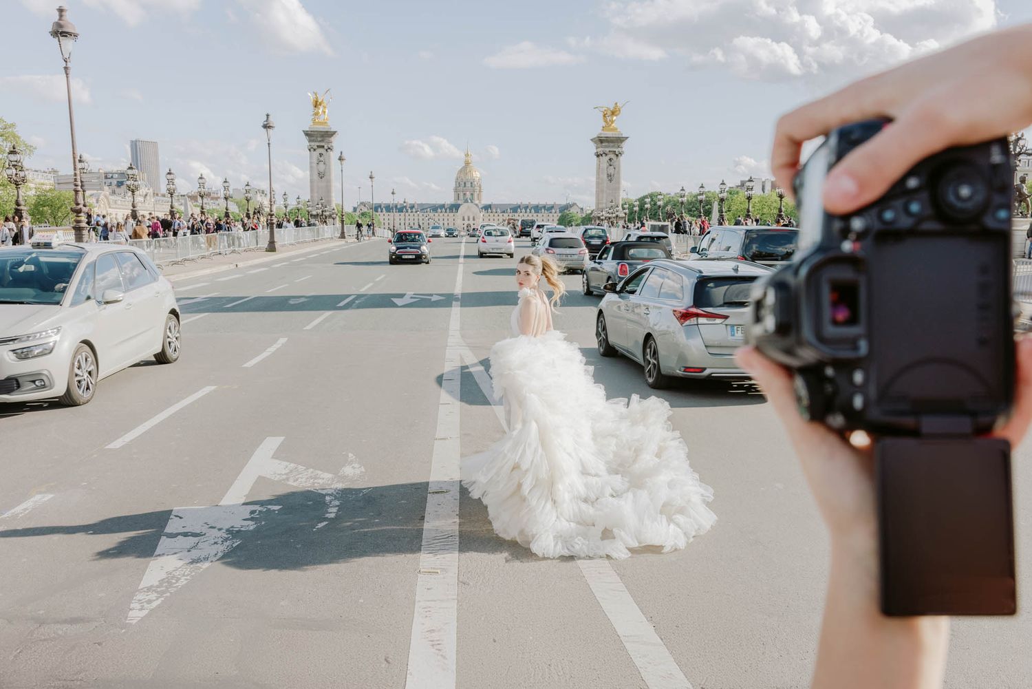 Photographer capturing bride in white gown walking on Paris bridge with traffic.