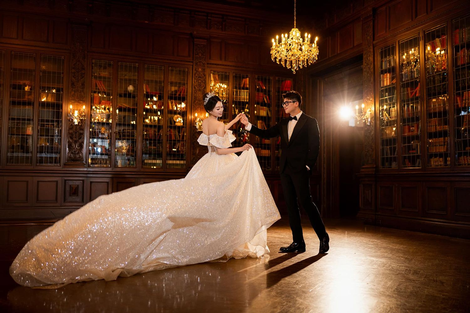 Bride and groom sharing a romantic dance in a grand library with golden chandelier lighting.