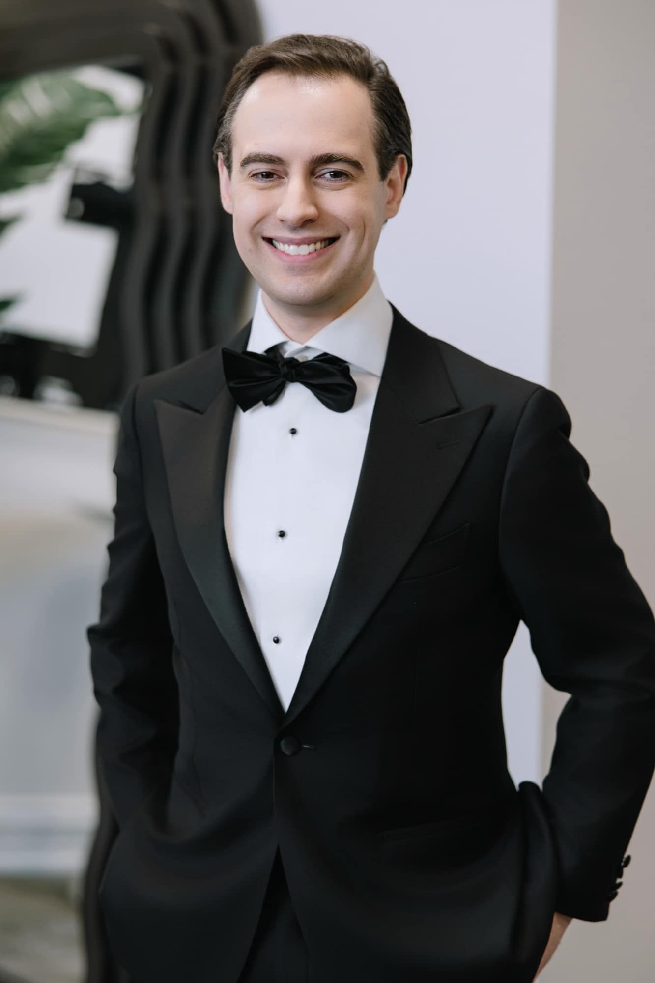 Handsome groom smiling in a classic black tuxedo with bow tie, ready for his wedding day.