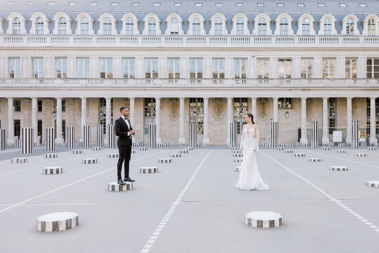 Bride and groom stand apart in a vast courtyard at the Palais Royal in Paris.