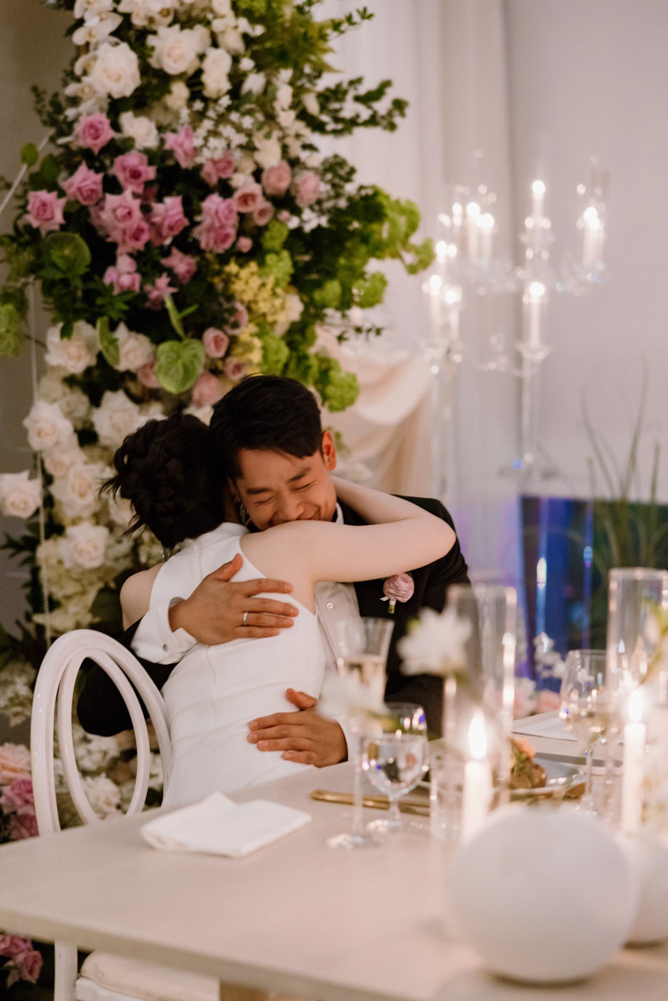 Bride and groom share an emotional embrace at their elegant candlelit wedding reception table.