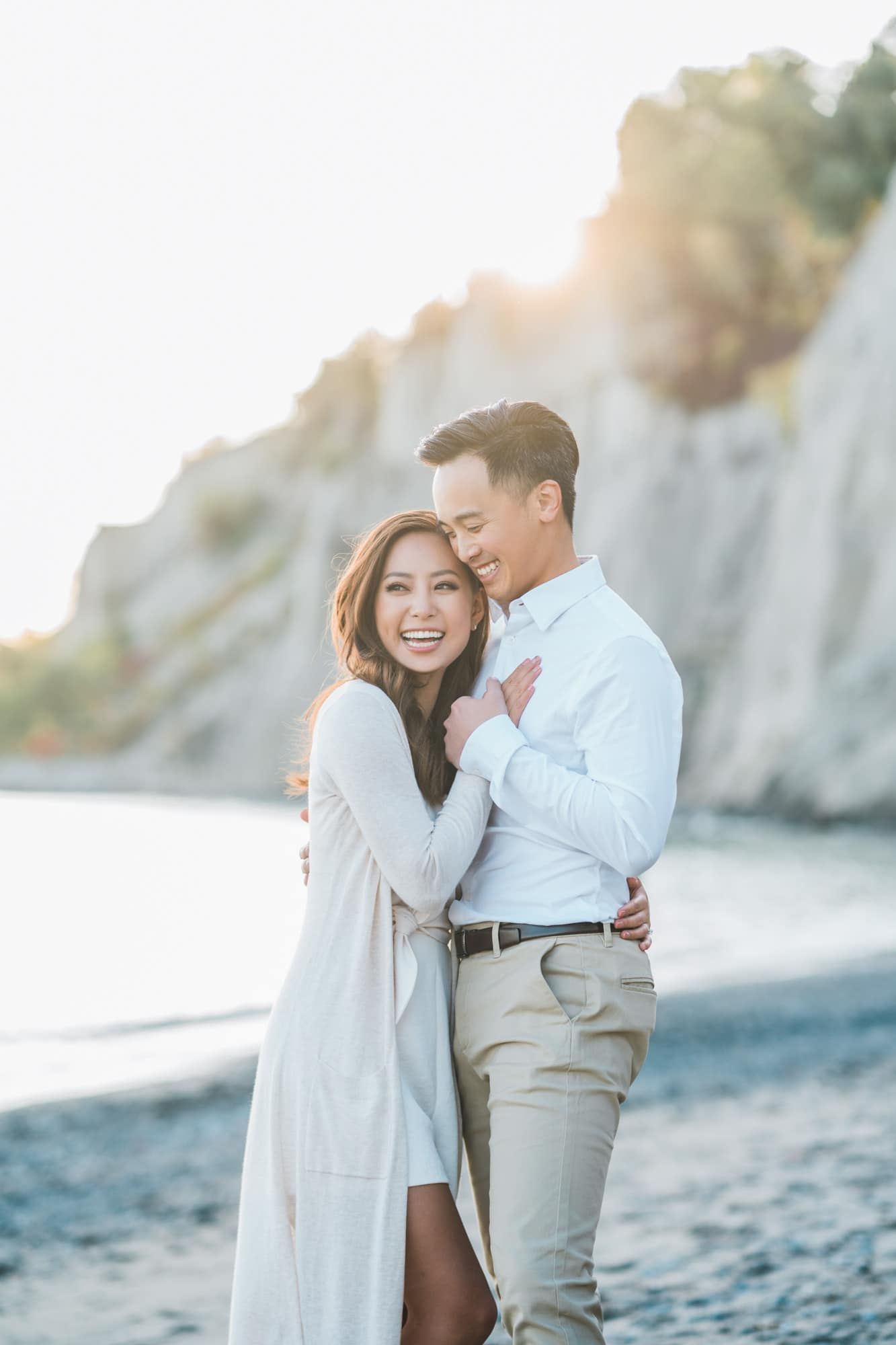 Joyful couple embracing on a rocky beach in warm golden sunlight.