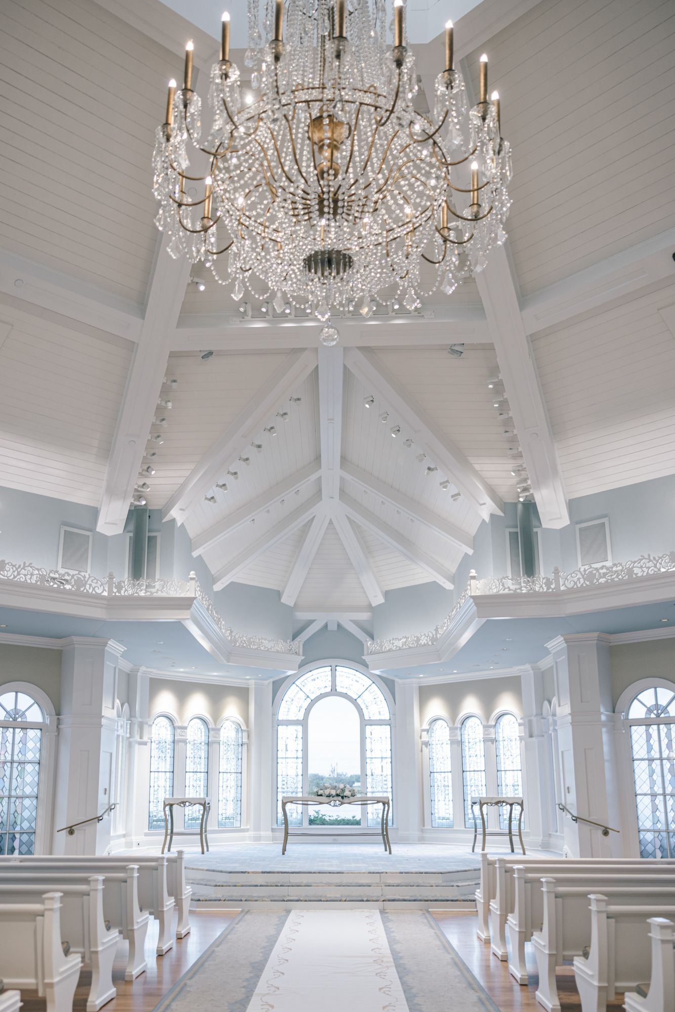 Elegant white wedding chapel interior featuring vaulted ceilings, arched windows, and a grand crystal chandelier.