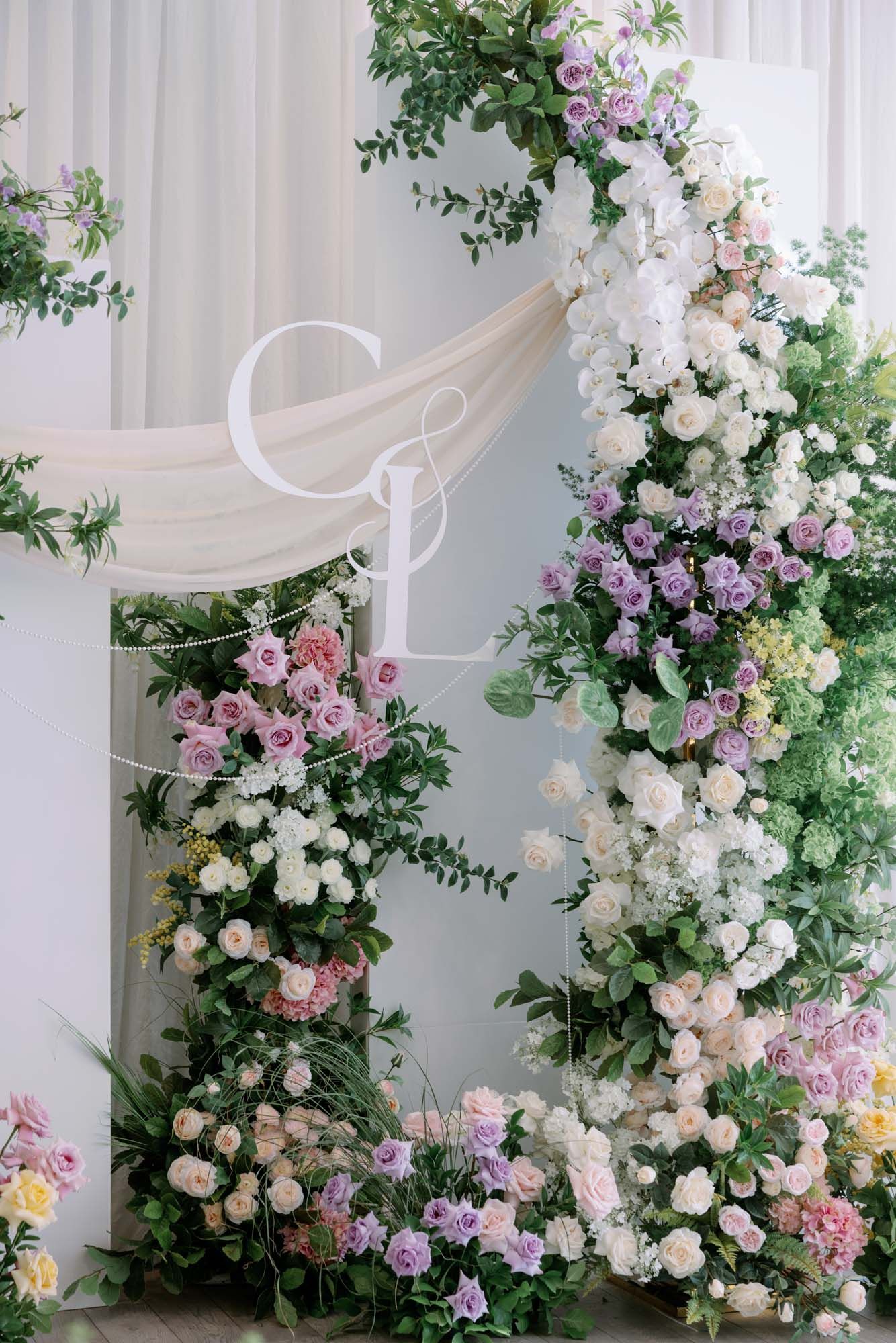 Close-up of a gorgeous wedding floral arch adorned with white, purple, and pink roses and greenery.