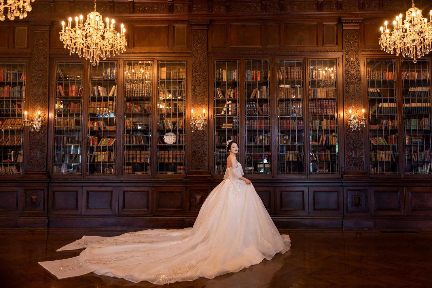 Bride in a voluminous ballgown posing in a warmly lit classic library with floor-to-ceiling bookshelves.