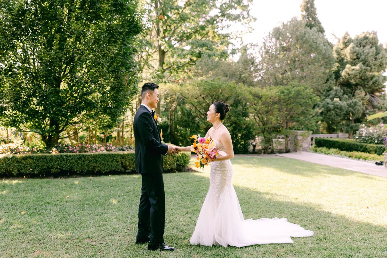 Couple sharing a first look moment on a green lawn holding a colorful bouquet.
