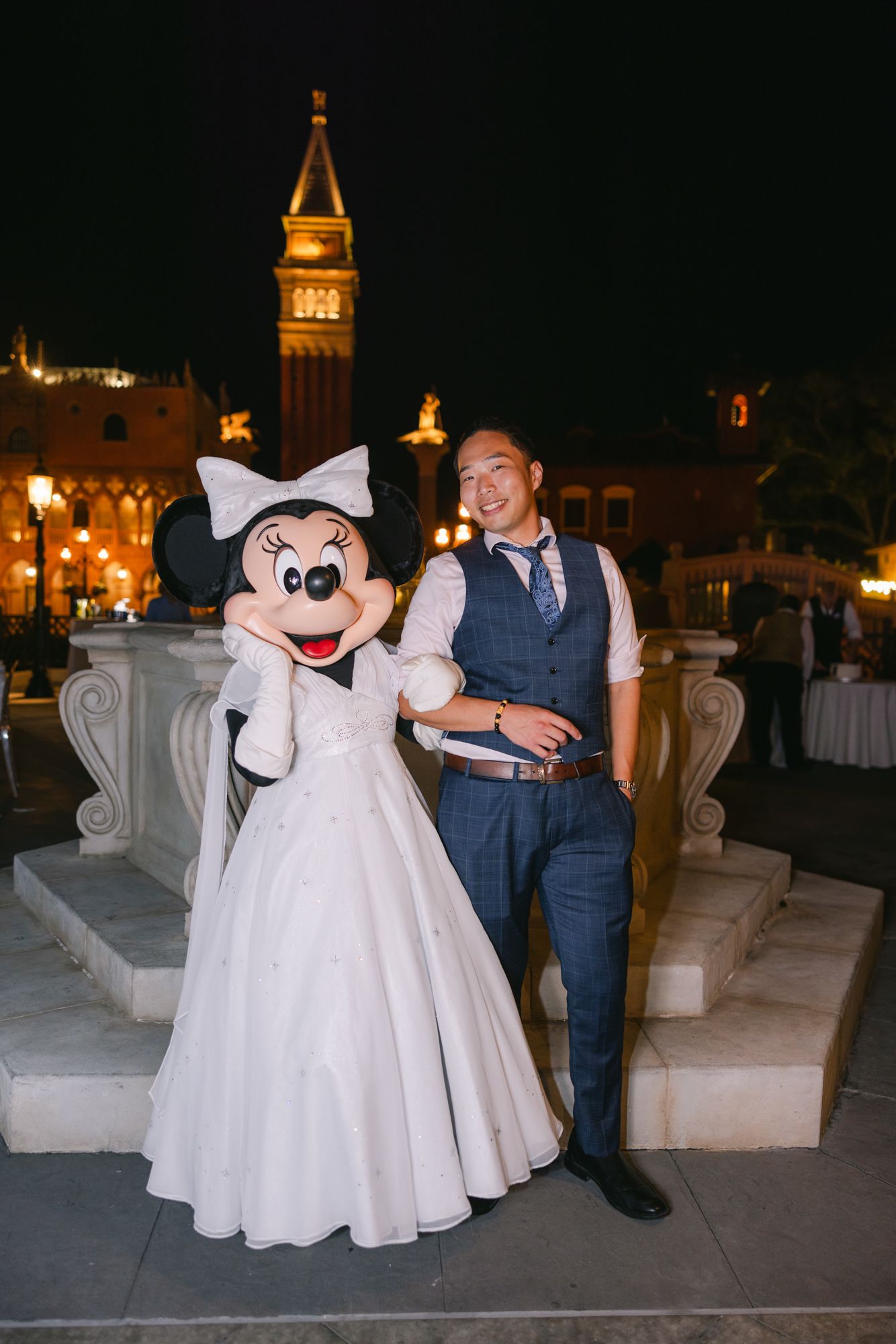 Groom posing with Minnie Mouse in a white wedding gown at Disney World EPCOT at night.