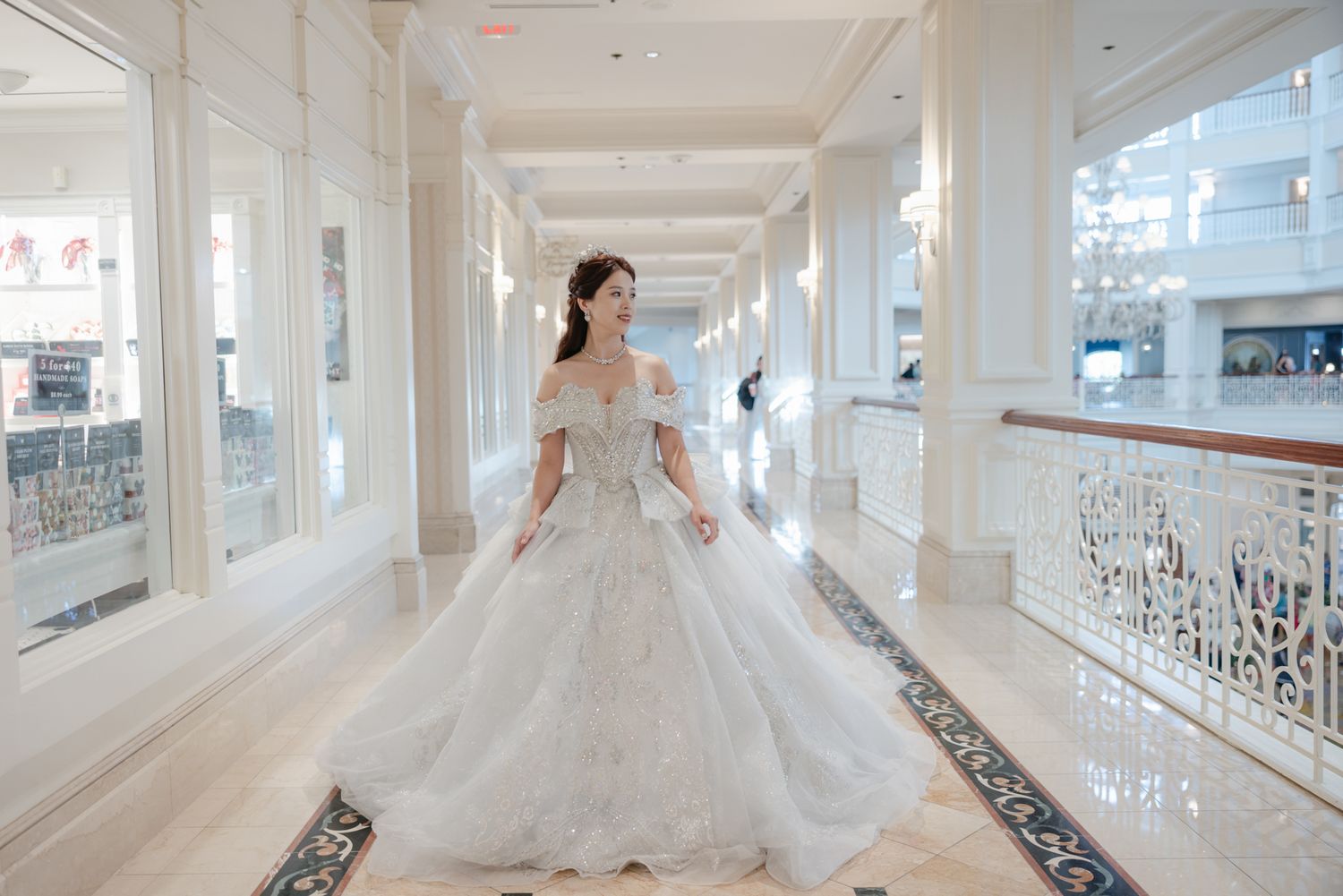 A bride in a stunning embellished ballgown walks through a luxurious white marble hallway with chandeliers above.