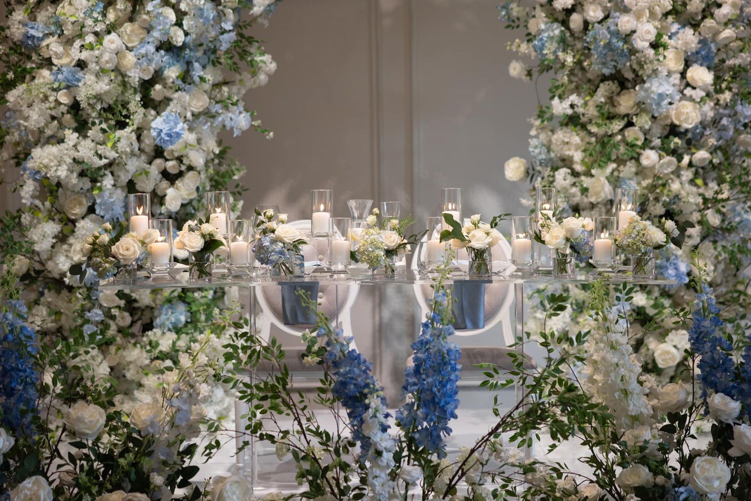 Stunning blue and white floral wedding reception tablescape with hydrangeas, roses, and candles.