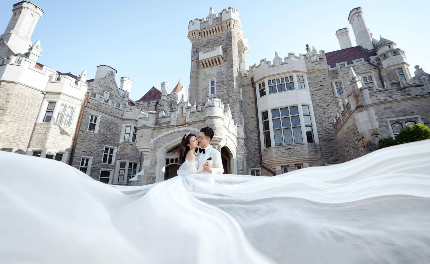 Wedding couple embraces in front of the grand stone facade of Casa Loma castle.