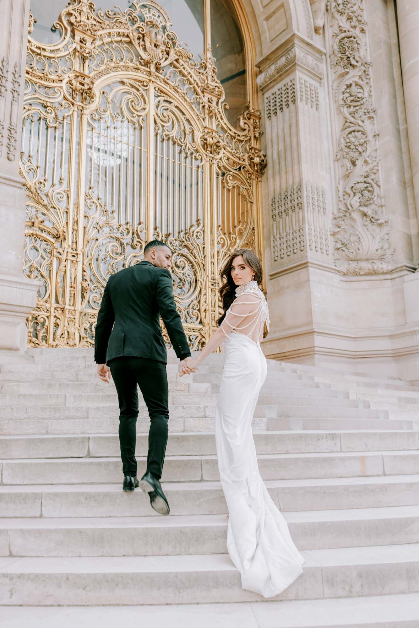 Elegant couple climbing steps before ornate golden gates at San Francisco City Hall.