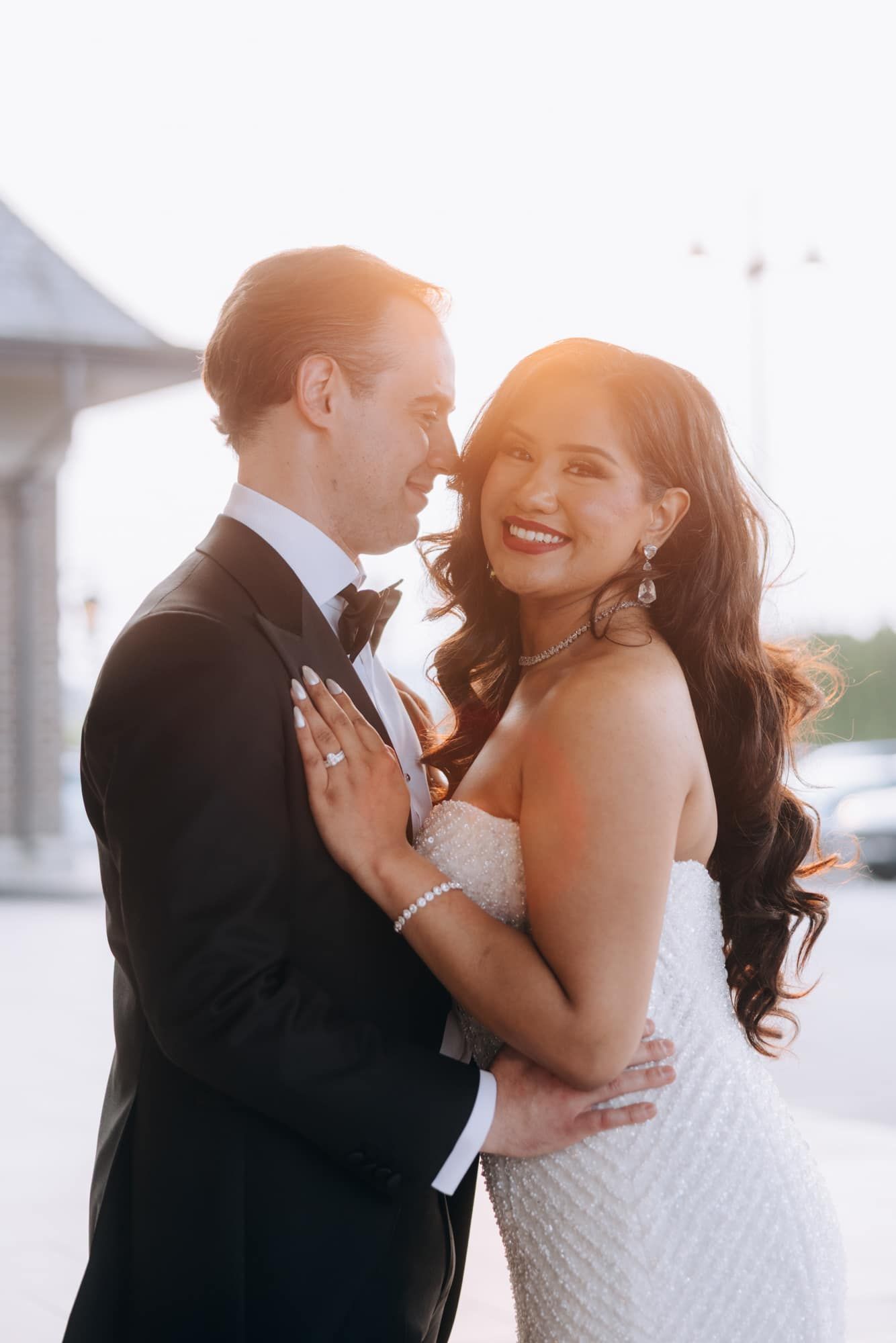 Smiling bride and groom share a romantic embrace bathed in warm golden sunset light.