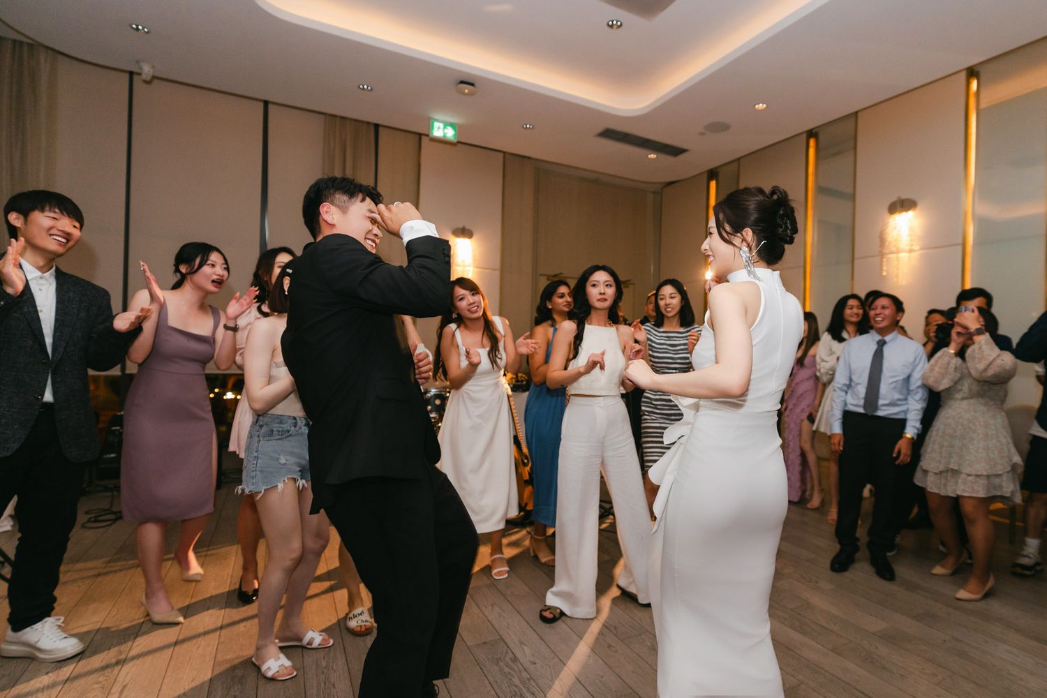 Bride and groom share first dance surrounded by clapping guests at elegant wedding reception.