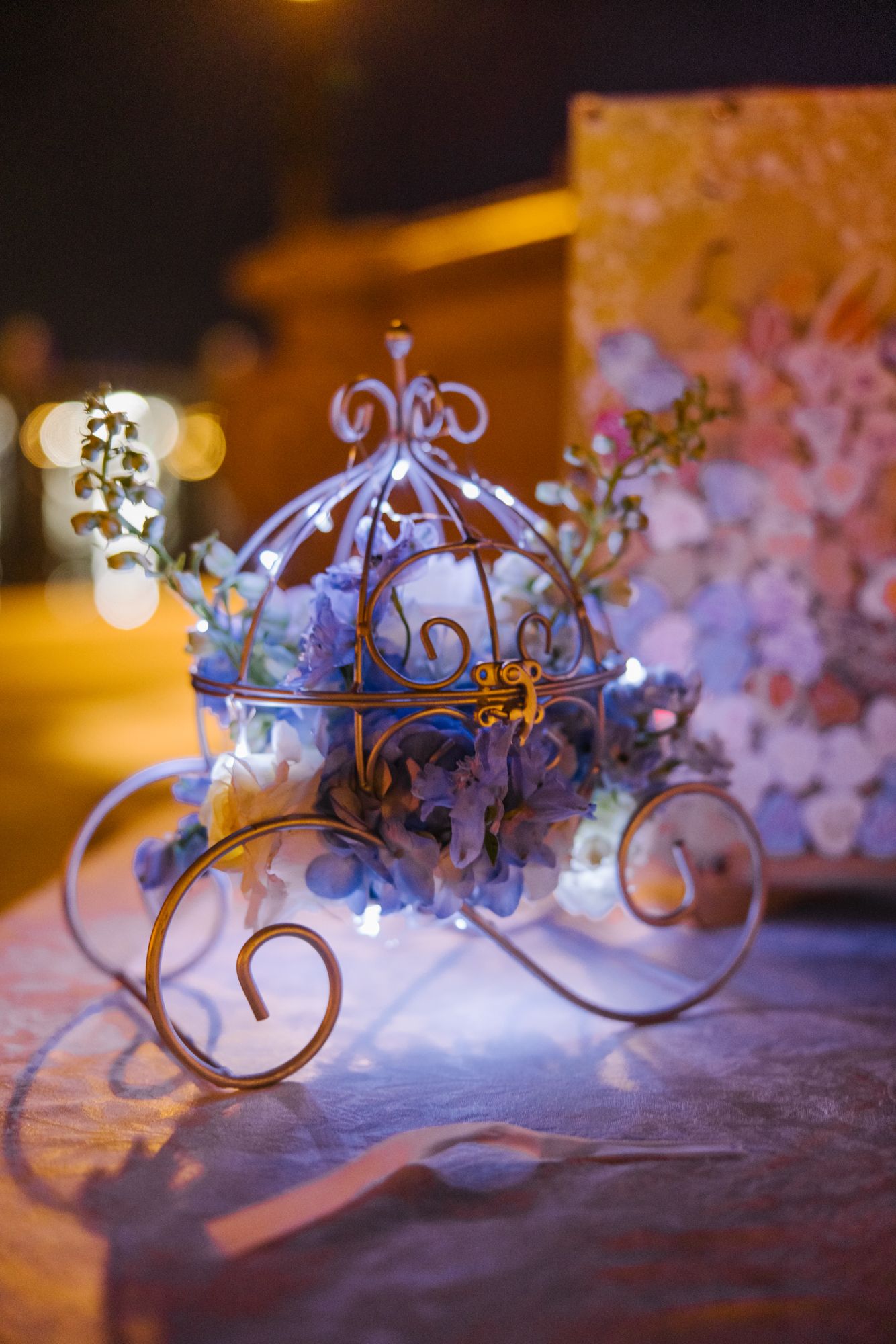Decorative Cinderella carriage centerpiece with blue flowers and fairy lights glowing at night event.