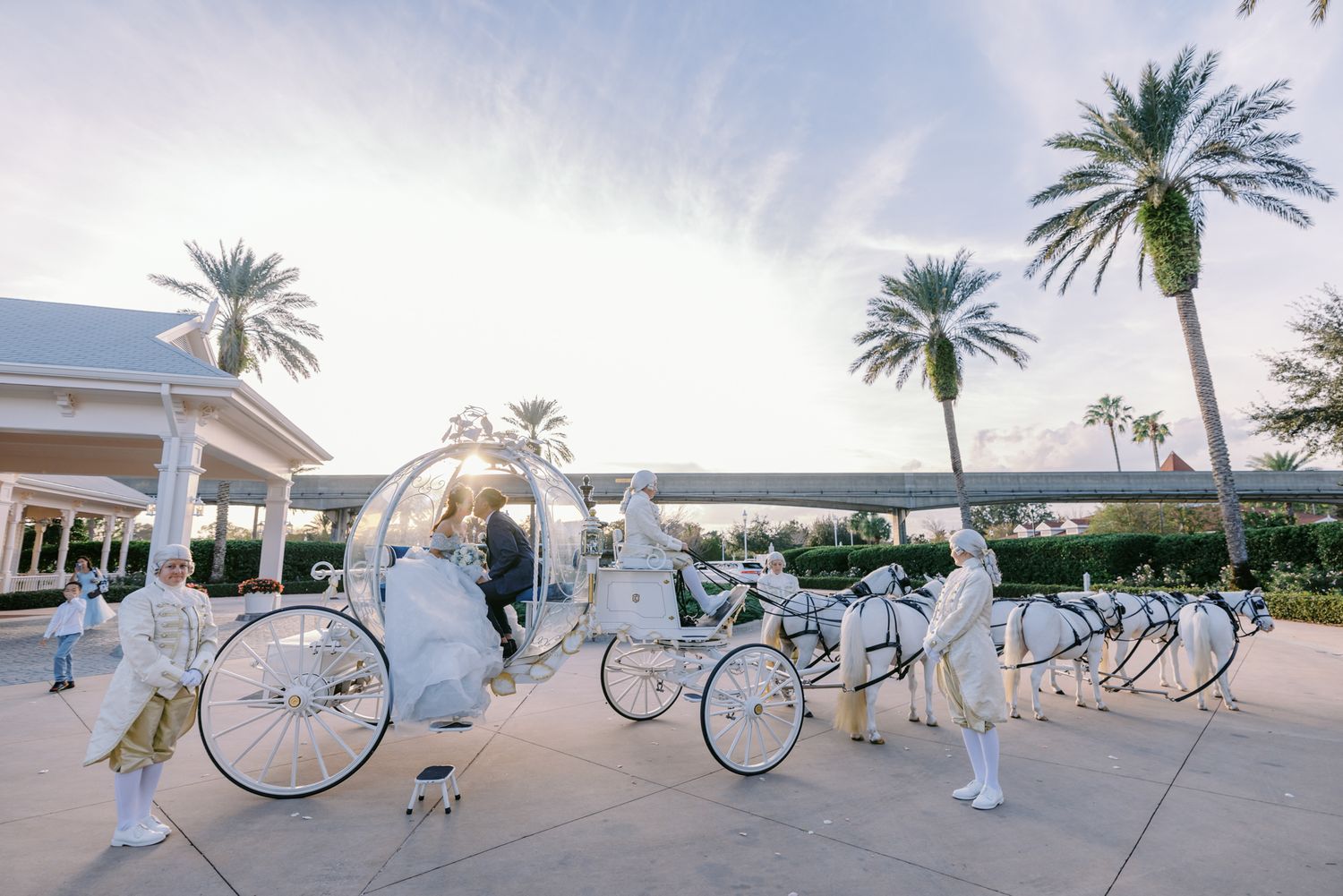 Elegant white Cinderella carriage with horses at a Disney fairy tale wedding ceremony outdoors with palm trees.