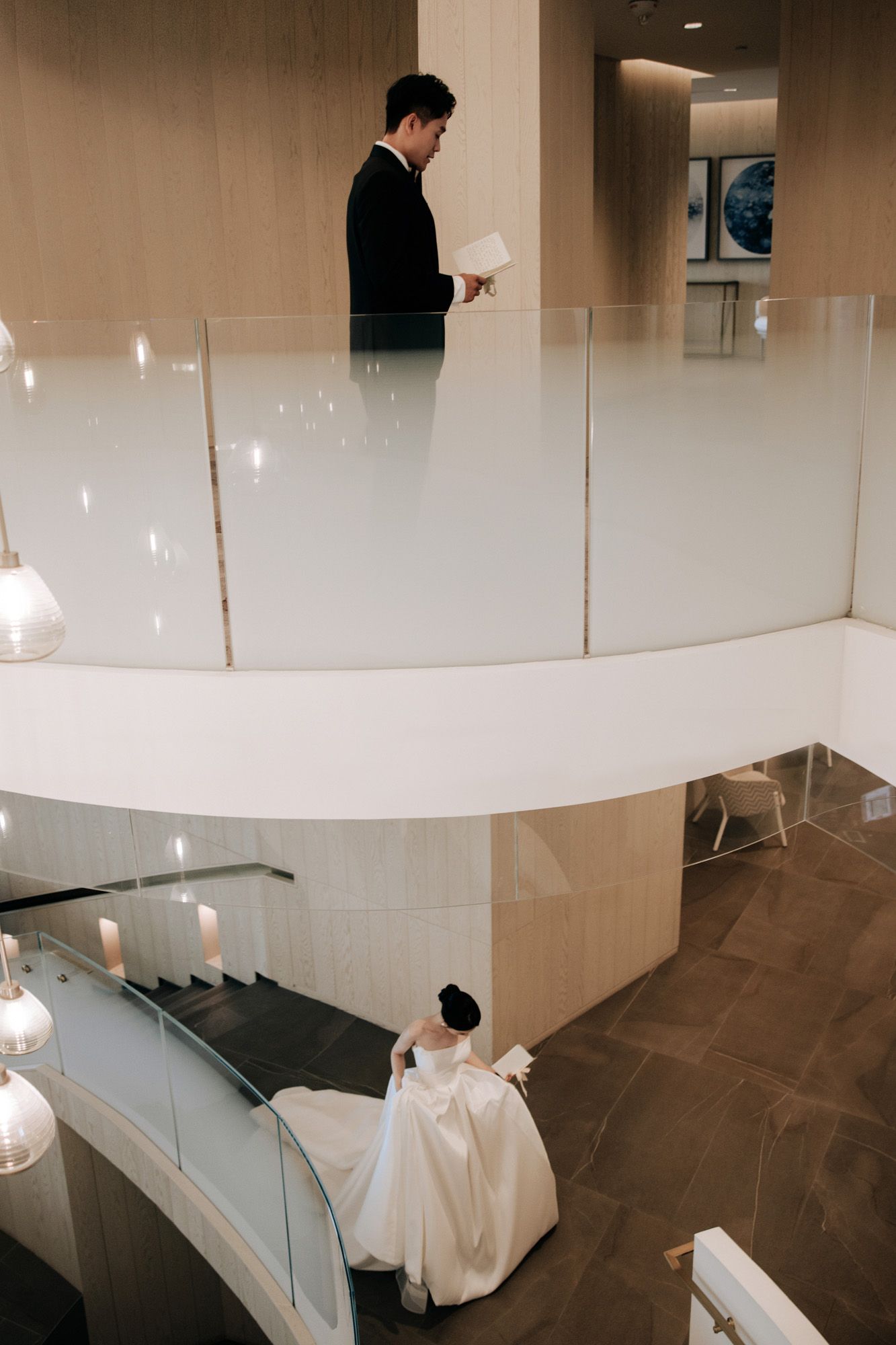 Bride and groom read vows letters separately on different levels of a modern spiral staircase.