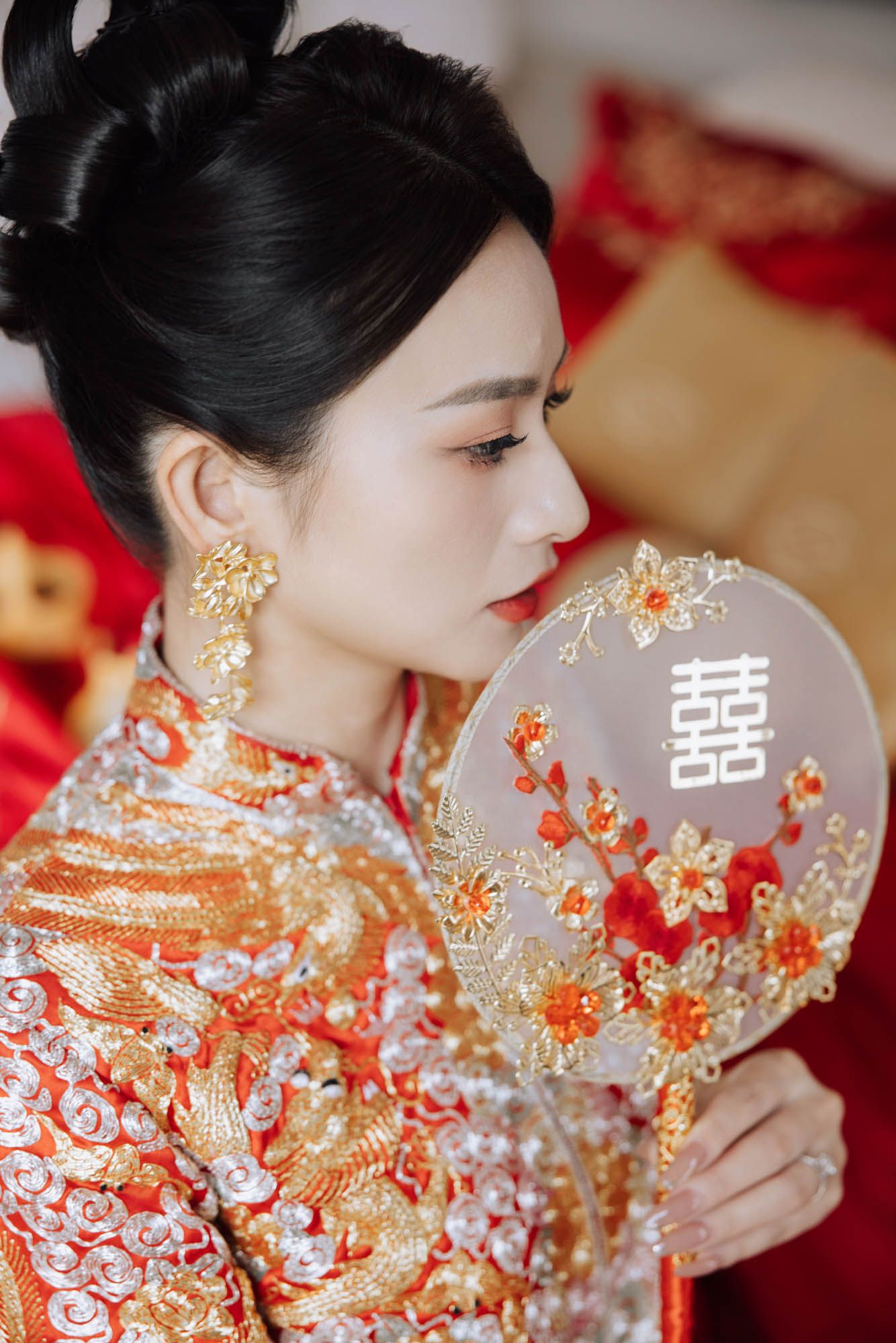 Chinese bride in traditional red embroidered qipao holding a decorative double happiness fan.