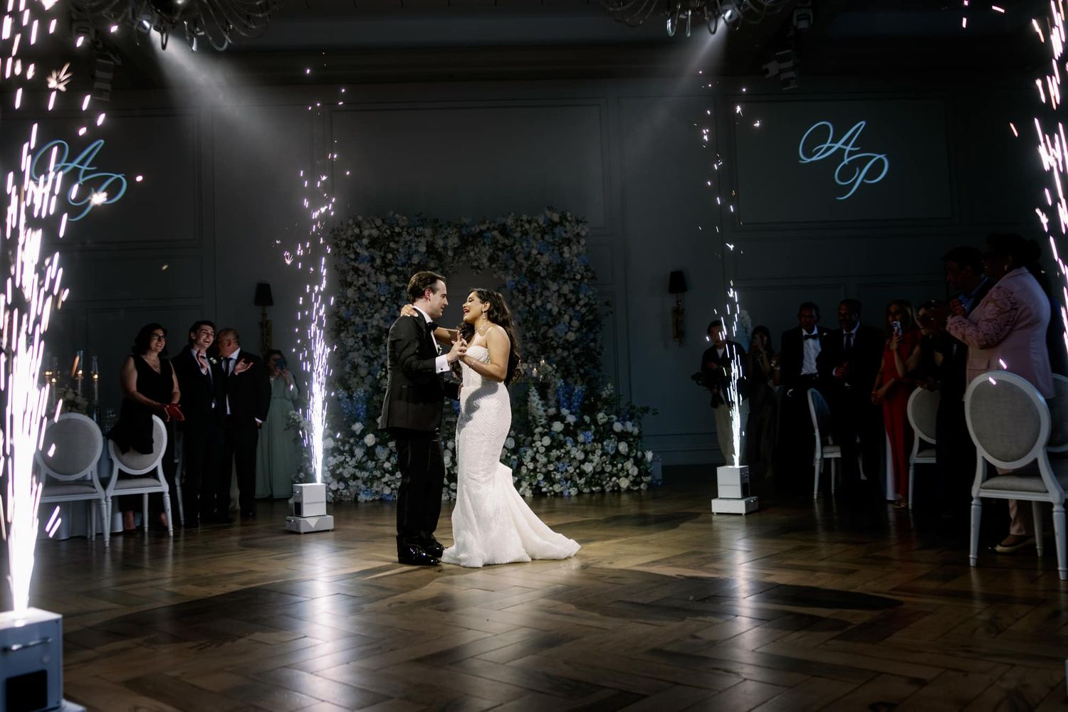 Couple shares romantic first dance with fireworks and floral backdrop at luxury wedding reception.
