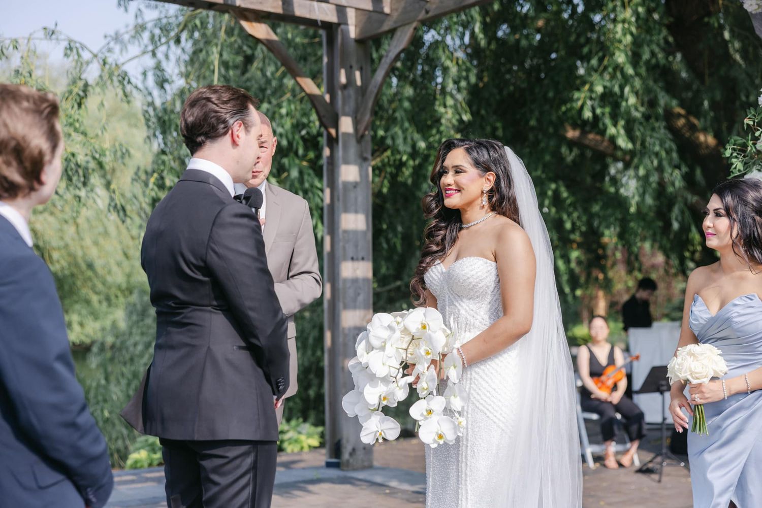 Bride smiles lovingly at groom during intimate outdoor garden wedding ceremony with veil.
