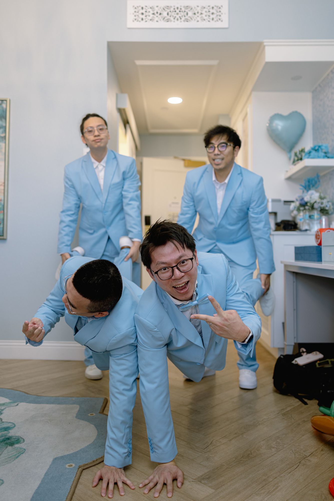 Four groomsmen in matching light blue suits posing playfully in modern apartment before wedding.