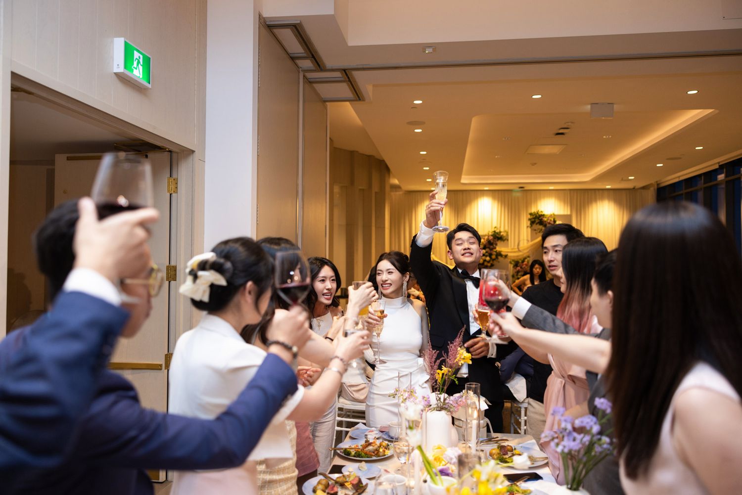 Joyful wedding reception toast with bride groom and guests raising glasses in celebration.