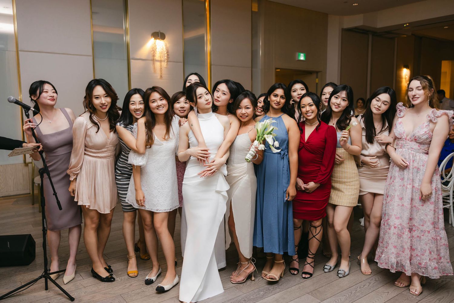 Bride poses with a large group of smiling female wedding guests after the bouquet toss ceremony.