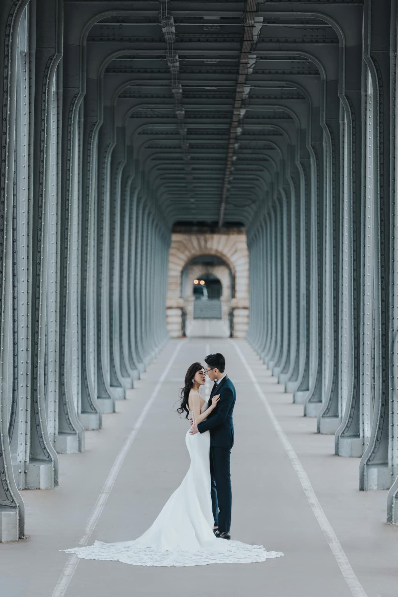 Bride and groom embracing under symmetrical steel arches of Bir-Hakeim Bridge Paris.