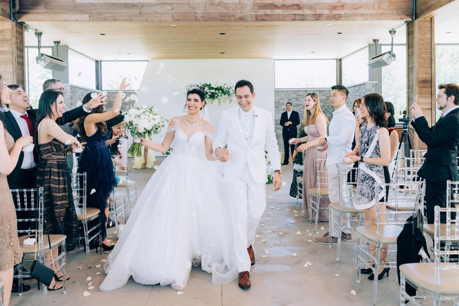Bride and groom celebrate recessional amid confetti in modern sunlit wedding venue.