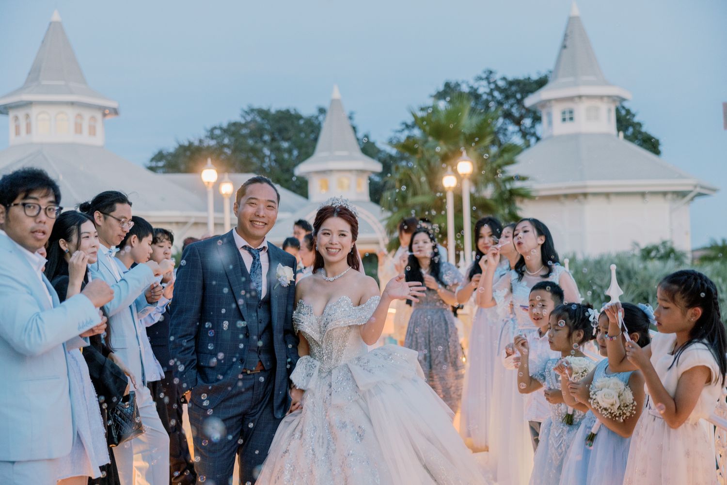 Newlyweds exit chapel surrounded by cheering guests with sparklers at twilight outdoor Disney wedding celebration.