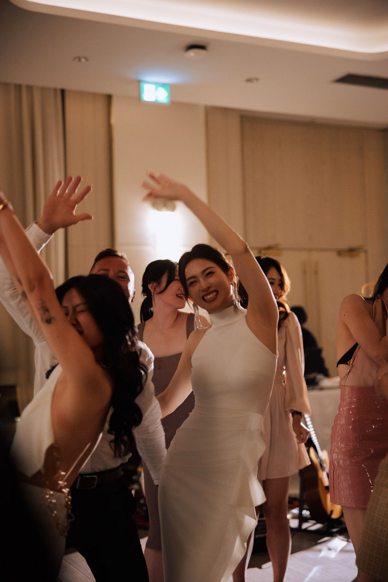 Radiant bride in white halter dress dances and smiles with guests during lively wedding reception celebration.