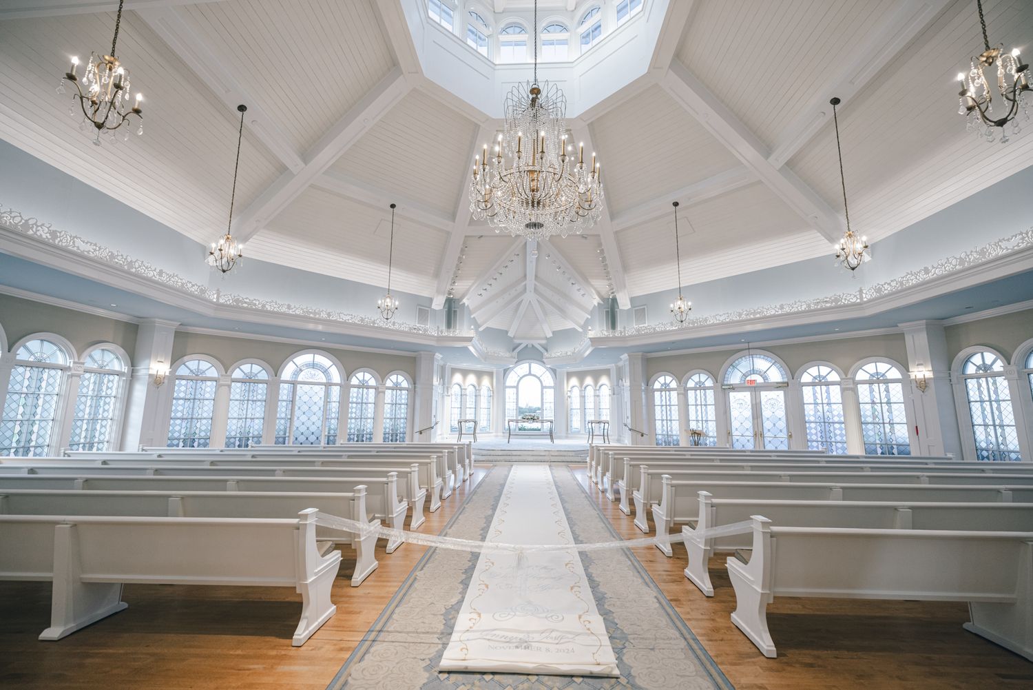 Bright white wedding chapel interior with crystal chandelier, pews, and skylight above altar.