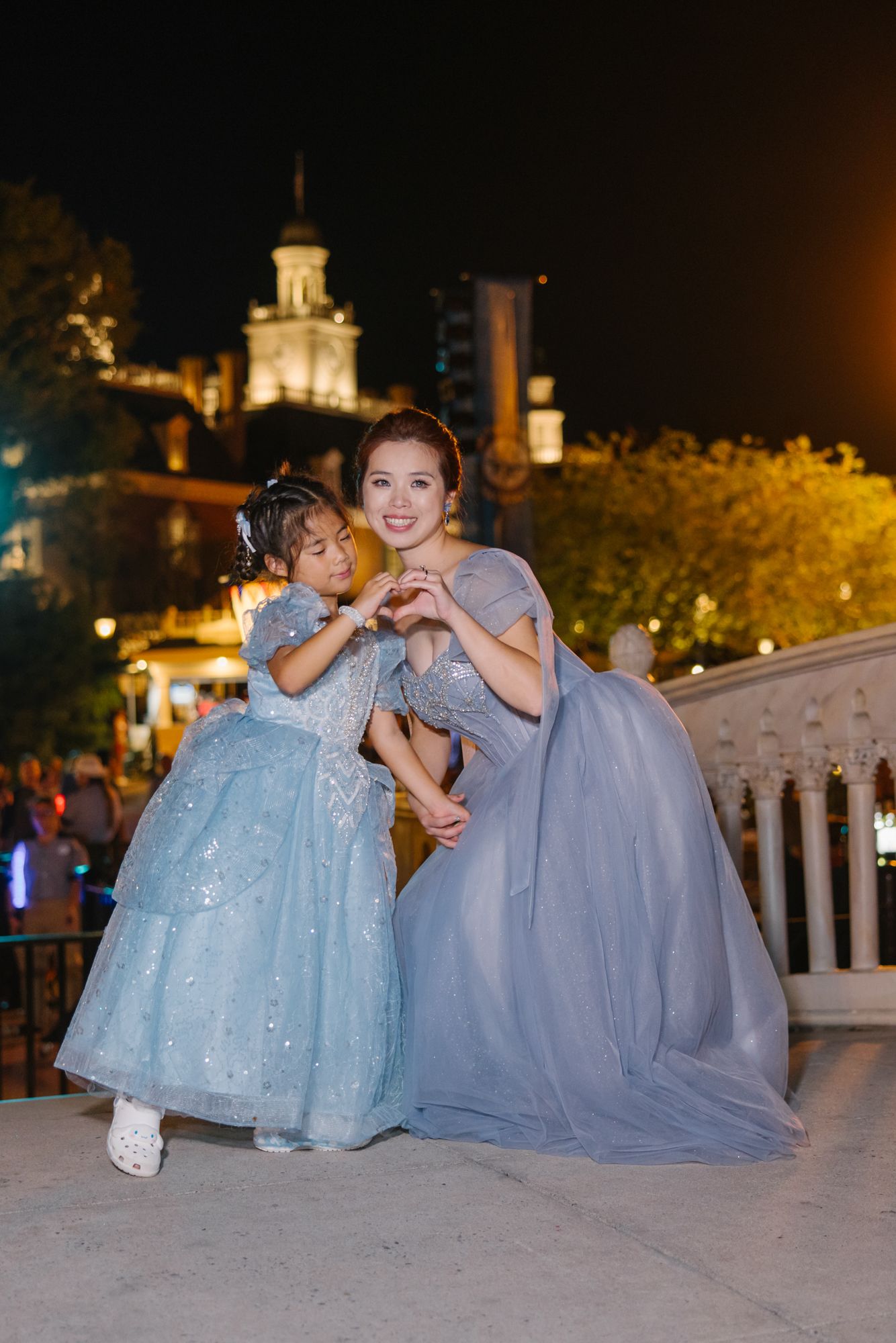 Bride in blue gown posing with young flower girl in matching Elsa dress at Disney World at night.