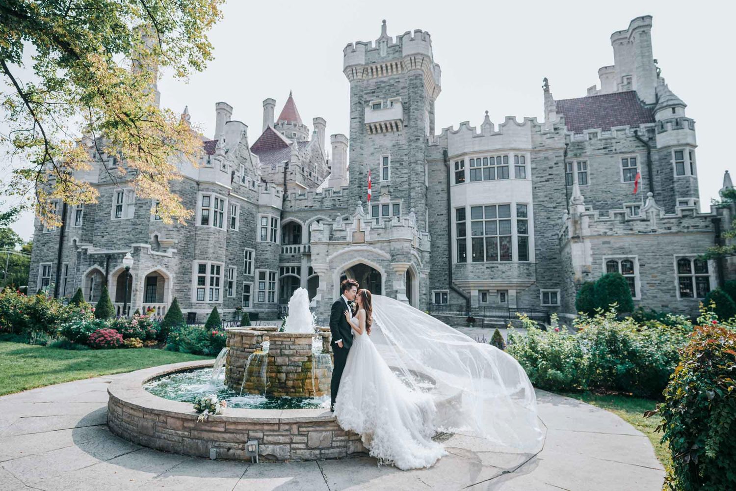 Wedding couple shares a romantic moment by a fountain with a stunning castle backdrop outdoors.