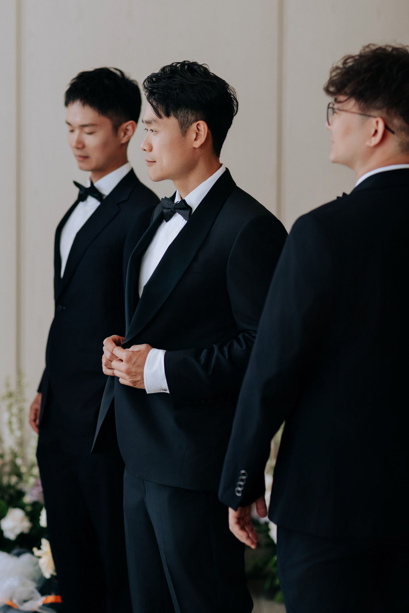 Three groomsmen in black tuxedos with bow ties stand at the wedding altar.