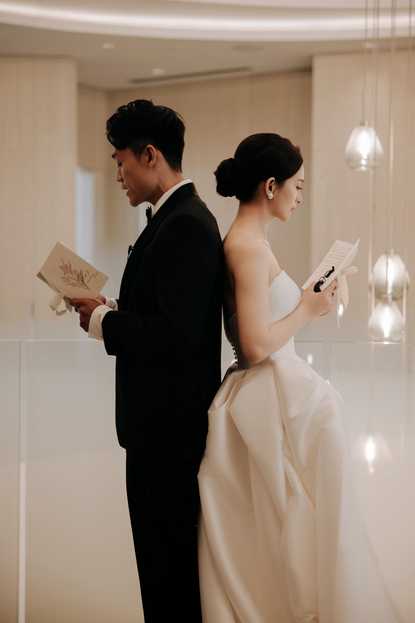 Bride and groom stand back-to-back reading heartfelt vow letters before their wedding ceremony.