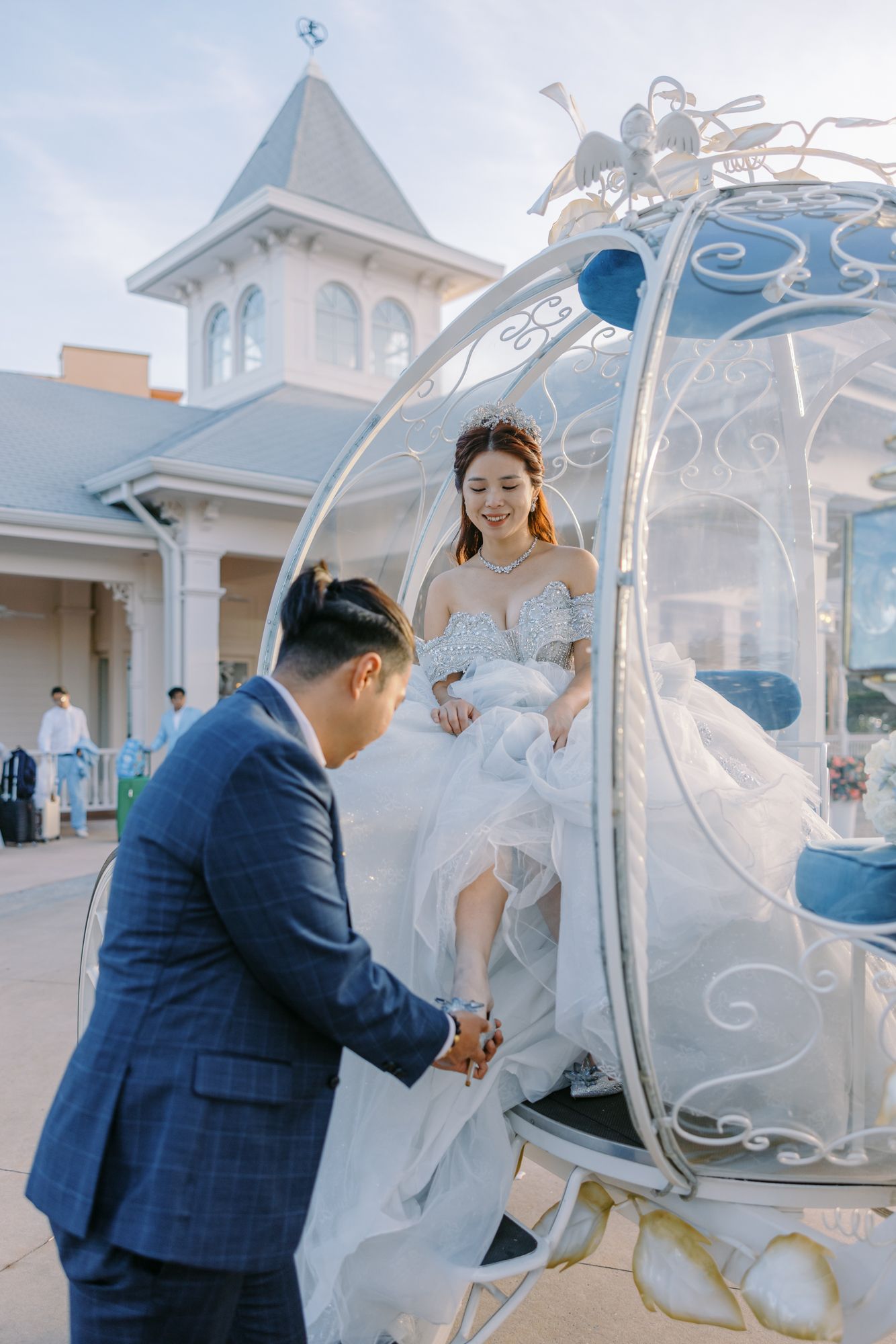 Groom helping bride in lace gown exit Cinderella carriage outside Disney wedding chapel.