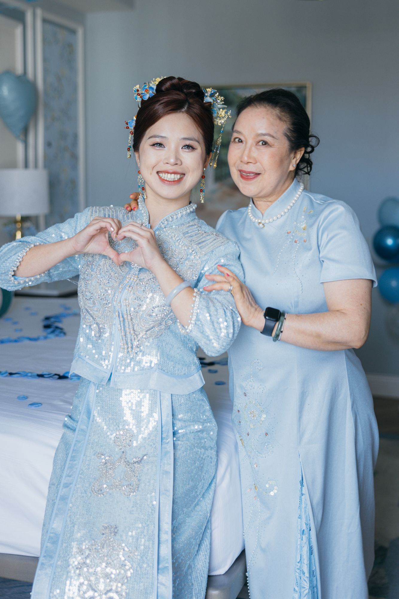 Two Vietnamese women in light blue ao dai traditional dresses making heart shape with hands.