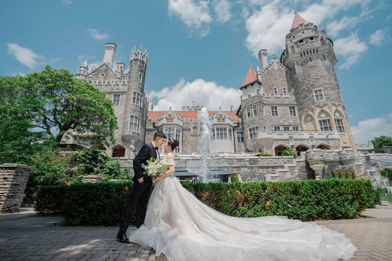 Wedding couple posing before Casa Loma castle in Toronto with bride in flowing gown.