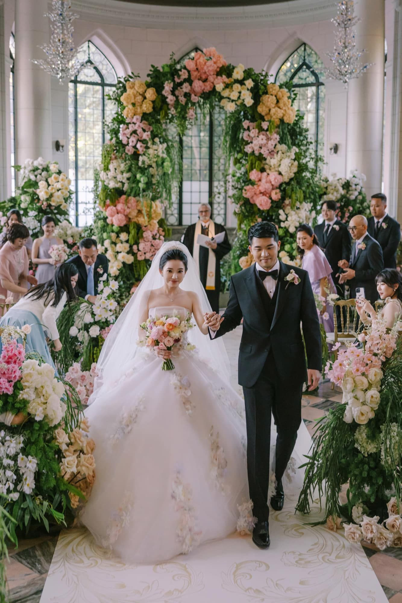 Bride and groom walking down aisle in floral-adorned chapel after romantic wedding ceremony.