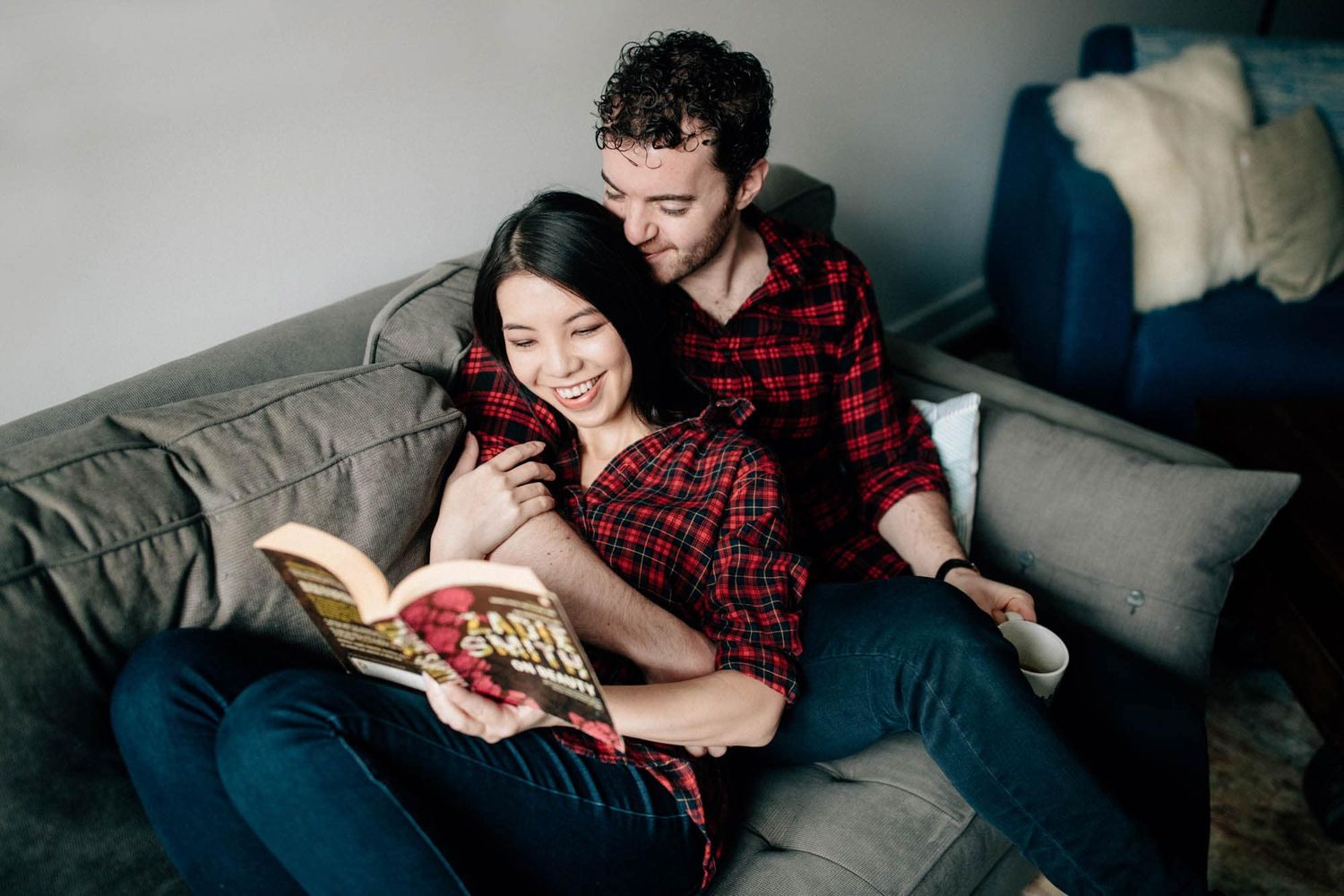 Cozy couple reading a book together on a gray sofa at home.