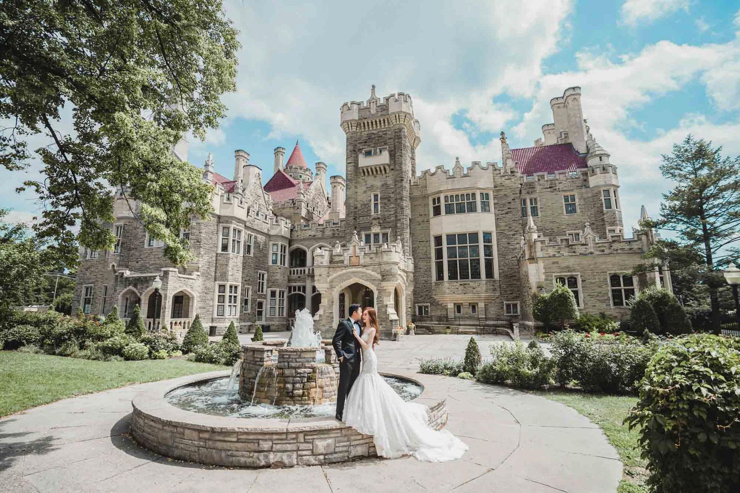 Bride and groom posing by fountain in front of stunning Casa Loma castle on wedding day.