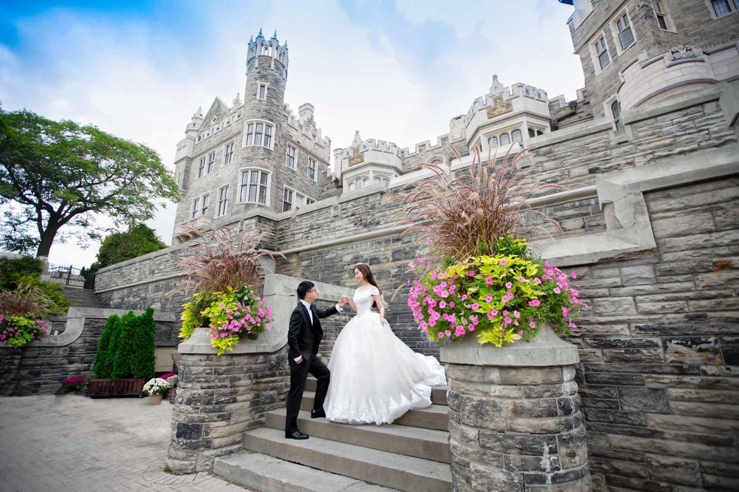 Bride and groom pose on castle steps adorned with vibrant floral arrangements on their wedding day.