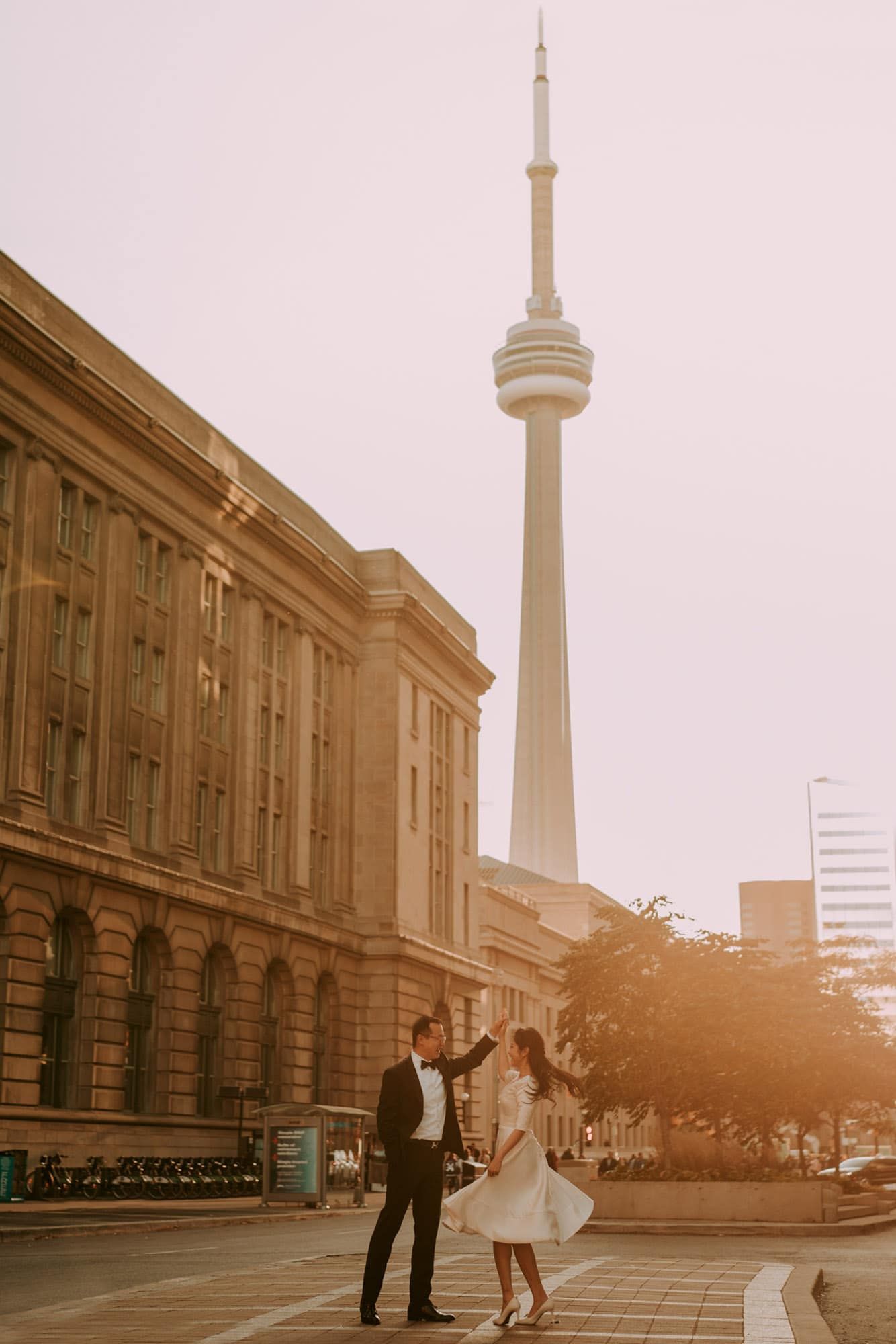 Bride and groom dancing joyfully in golden sunset light with the iconic CN Tower in Toronto behind them.