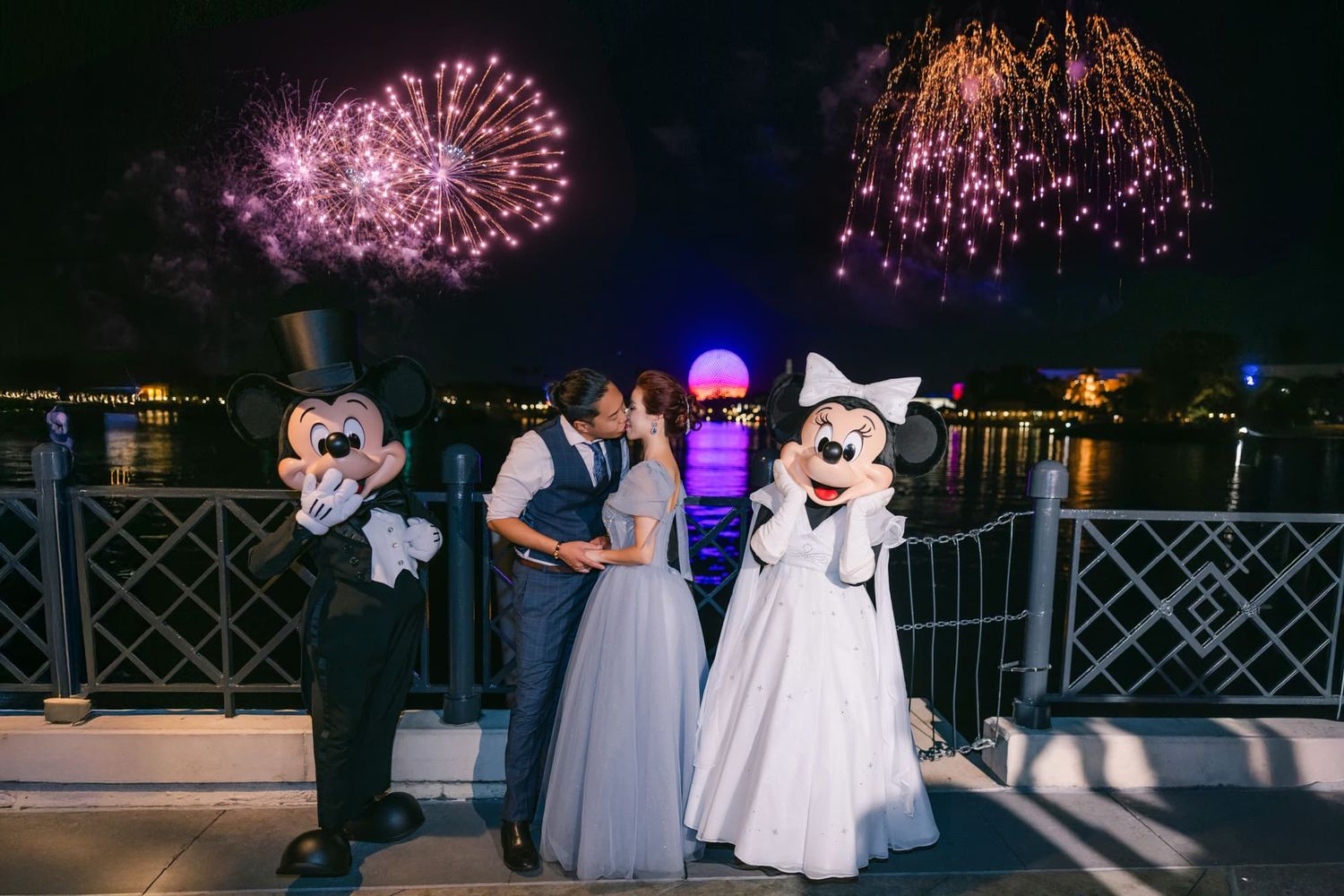 Couple kissing between Mickey and Minnie Mouse with colorful fireworks at Walt Disney World.